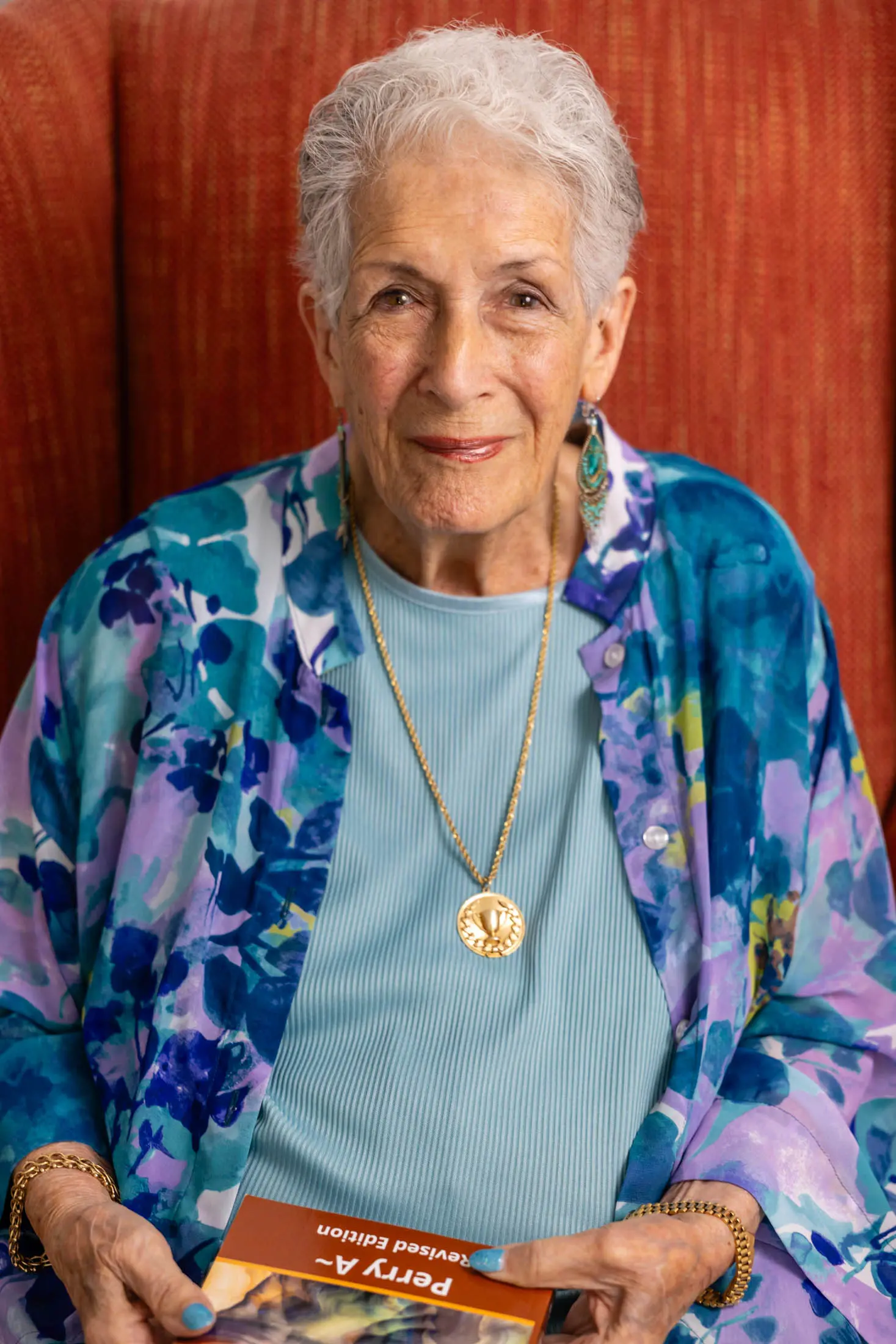 Portrait of a smiling elderly woman wearing a floral cardigan and gold necklace.