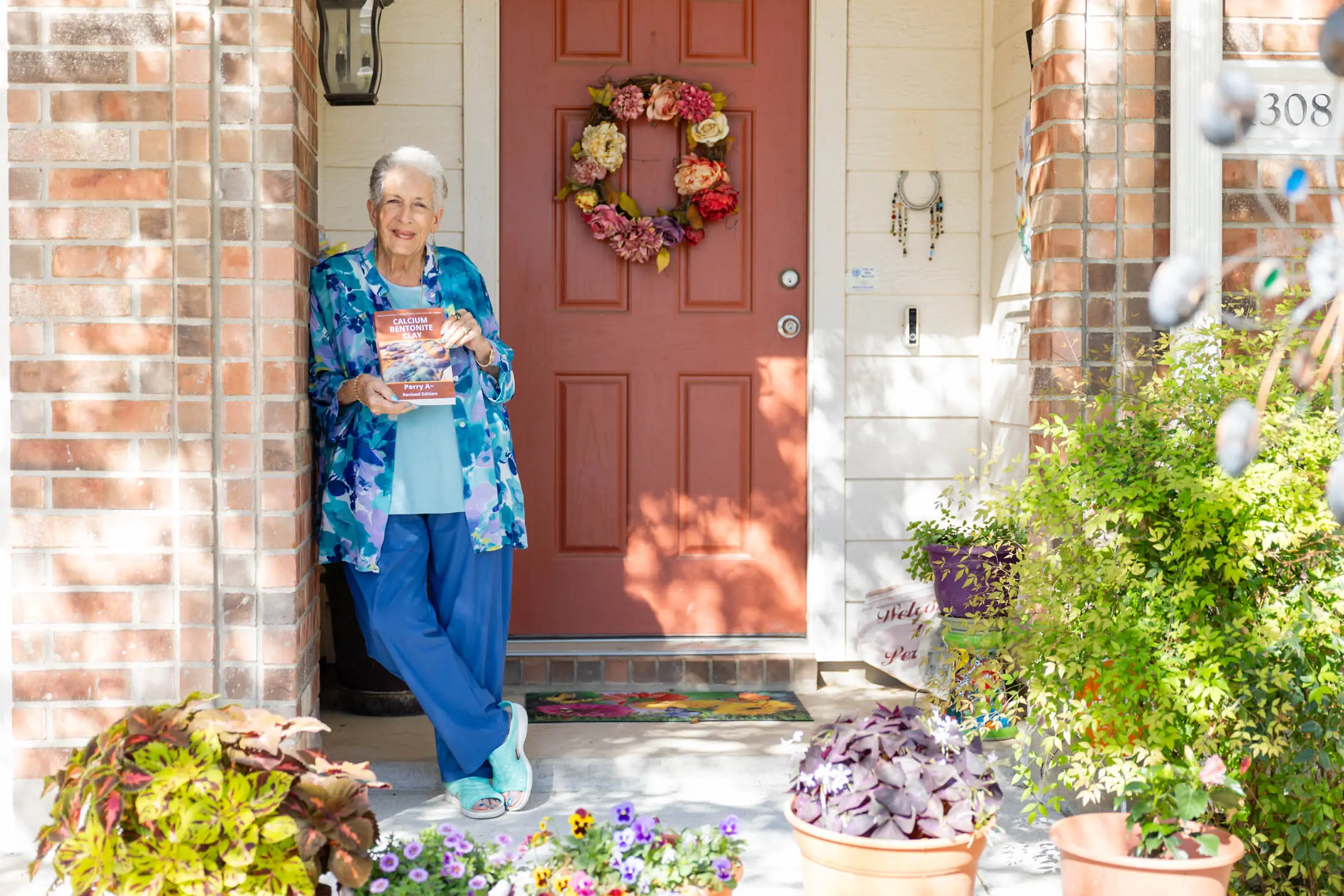 Elderly woman standing by her decorated front door with a smile.