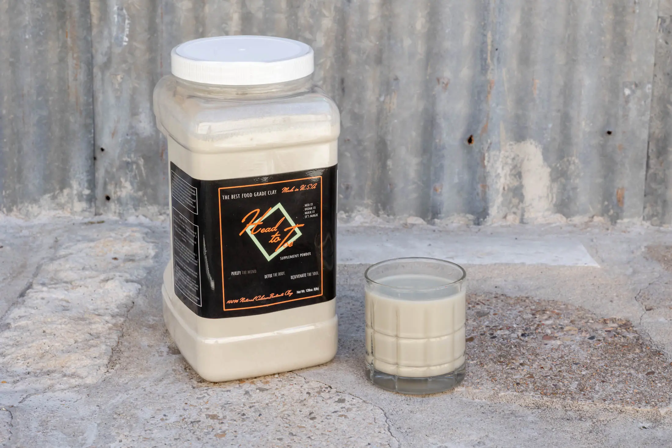 A jar of white powder and a glass of a white liquid on a concrete surface.